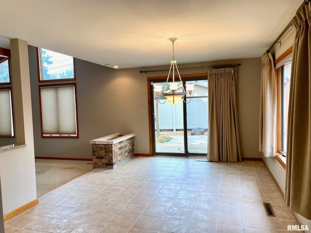 spare room featuring a notable chandelier, plenty of natural light, baseboards, and light tile patterned floors