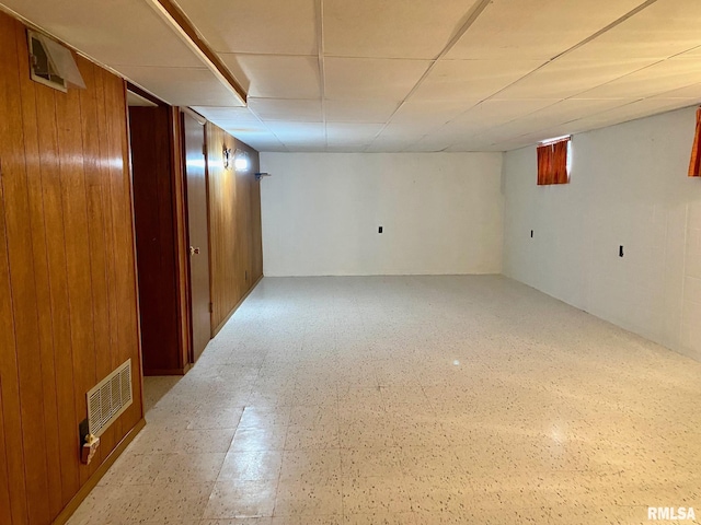 finished basement with visible vents, wooden walls, and tile patterned floors