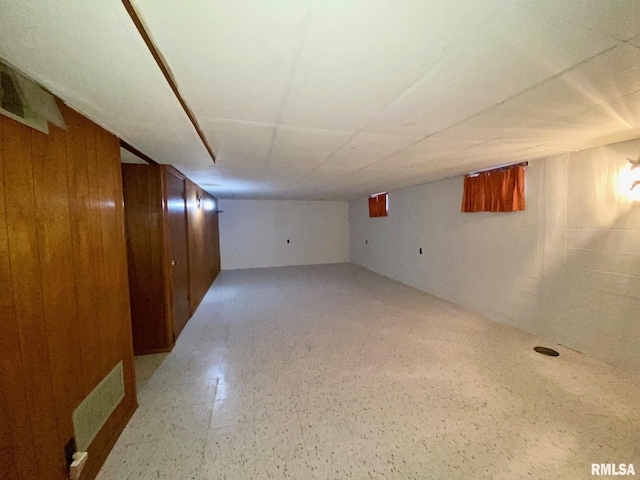 finished basement with visible vents, wood walls, and concrete block wall