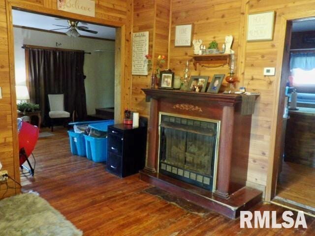 living area featuring wood walls, ceiling fan, wood finished floors, and a glass covered fireplace