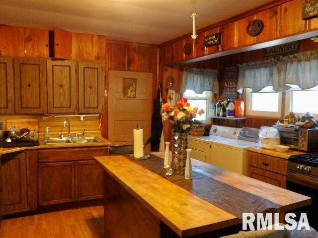 kitchen featuring brown cabinets, washing machine and clothes dryer, wooden counters, a sink, and stainless steel gas range oven