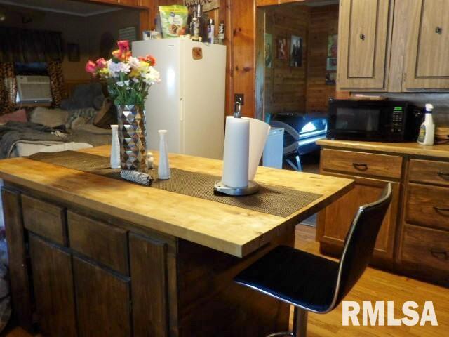 kitchen with light wood-style floors, butcher block countertops, black microwave, and freestanding refrigerator