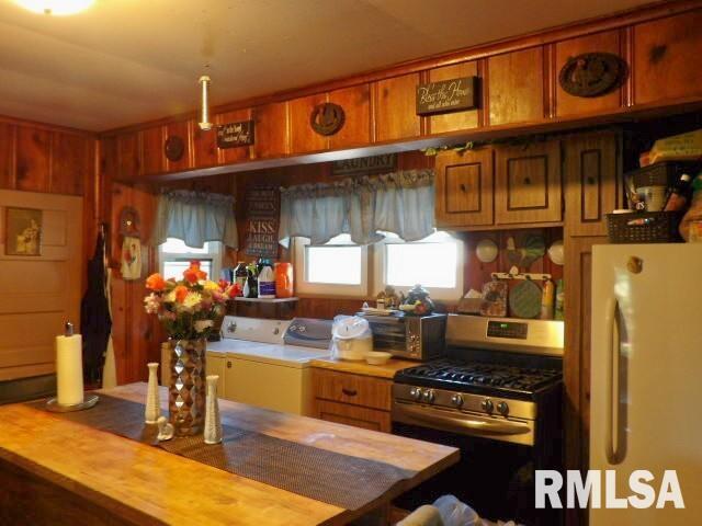 kitchen featuring brown cabinets, stainless steel gas range oven, washer and clothes dryer, and freestanding refrigerator