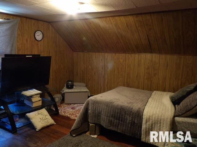 bedroom with wooden walls, vaulted ceiling, and wood finished floors