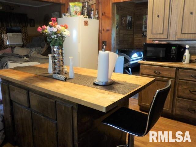 kitchen with black microwave, wood counters, freestanding refrigerator, and light wood-style floors