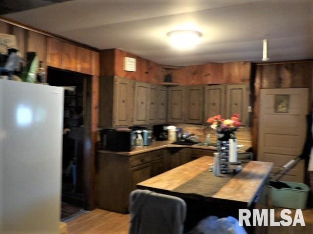 kitchen with light wood-style flooring, wood counters, freestanding refrigerator, and wooden walls