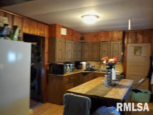 kitchen featuring freestanding refrigerator, brown cabinets, wooden walls, and light wood finished floors