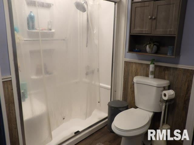 bathroom featuring a wainscoted wall, wood walls, a shower stall, and toilet