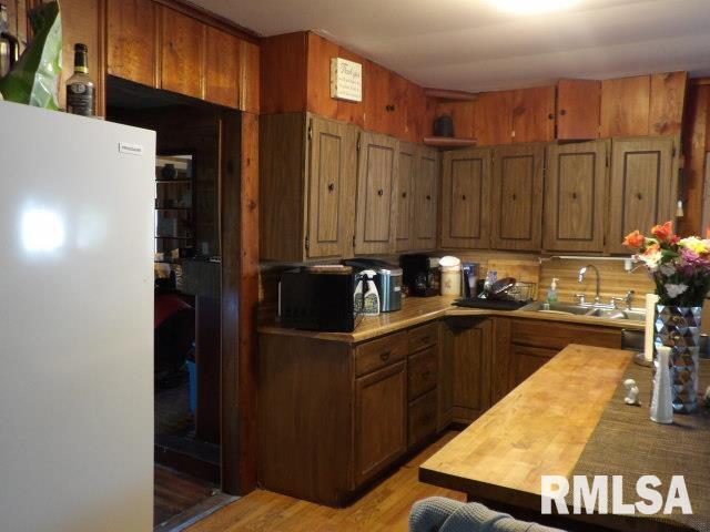 kitchen with brown cabinetry, freestanding refrigerator, a sink, and wood walls