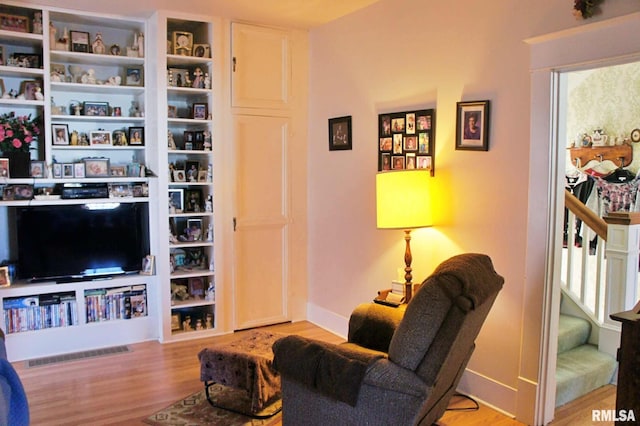 sitting room with stairs, visible vents, baseboards, and wood finished floors