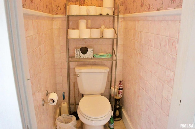 bathroom featuring a wainscoted wall, tile walls, toilet, and wallpapered walls