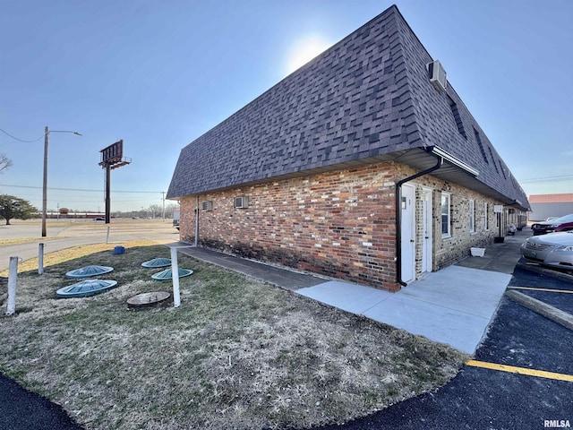 view of side of property with a shingled roof, mansard roof, and brick siding