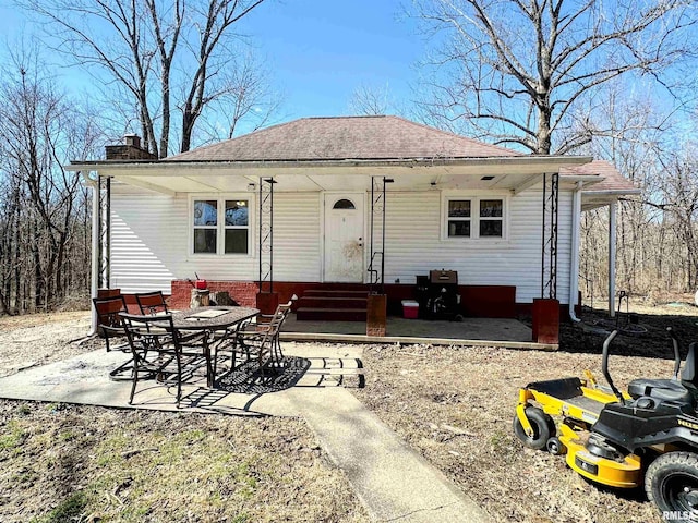 bungalow-style home with a shingled roof, entry steps, a patio area, and a chimney