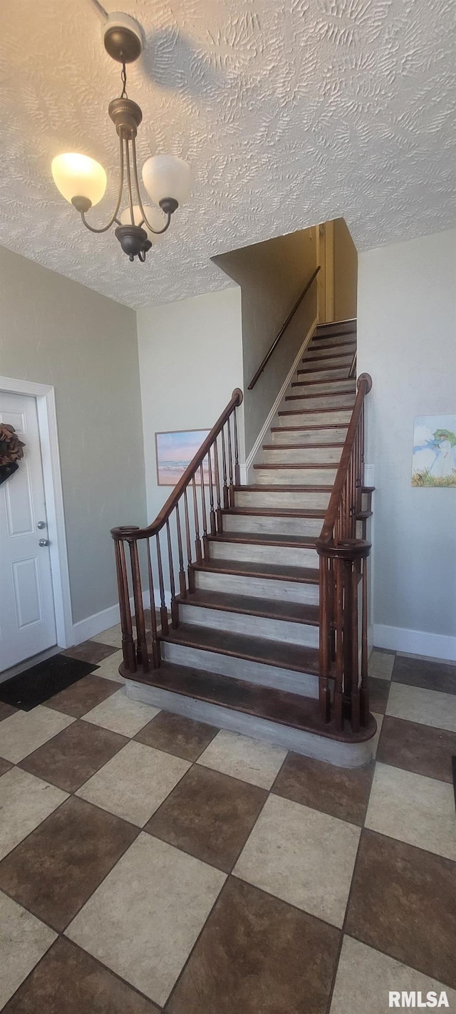 stairs with a textured ceiling, tile patterned floors, a notable chandelier, and baseboards