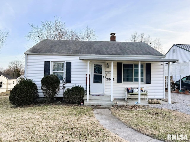 view of front of house featuring covered porch, roof with shingles, a chimney, and a front yard