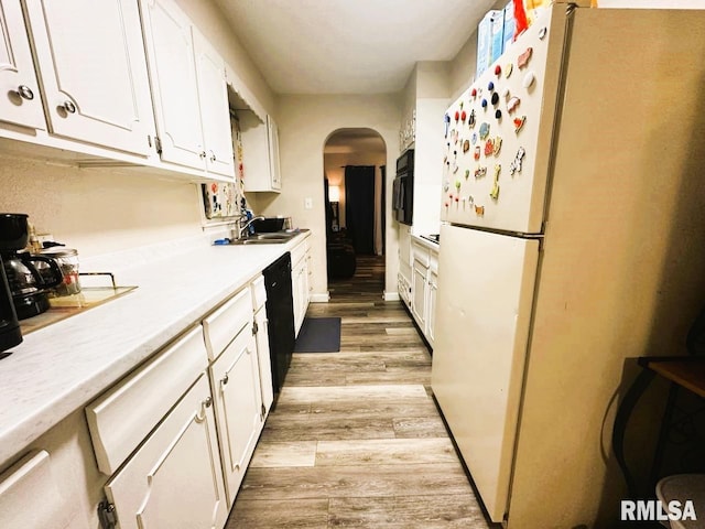 kitchen with light wood finished floors, arched walkways, white cabinets, freestanding refrigerator, and light countertops