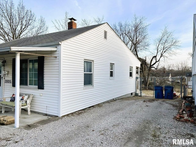 view of side of property with gravel driveway, a gate, a chimney, and fence