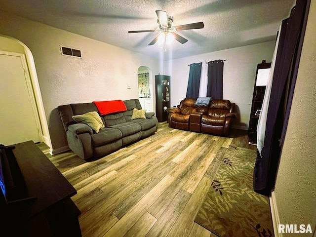 living room with arched walkways, a textured ceiling, wood finished floors, and visible vents