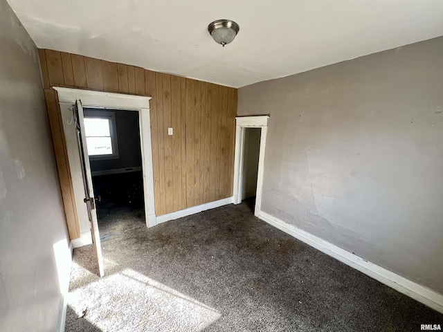 interior space with dark colored carpet, wood walls, and baseboards