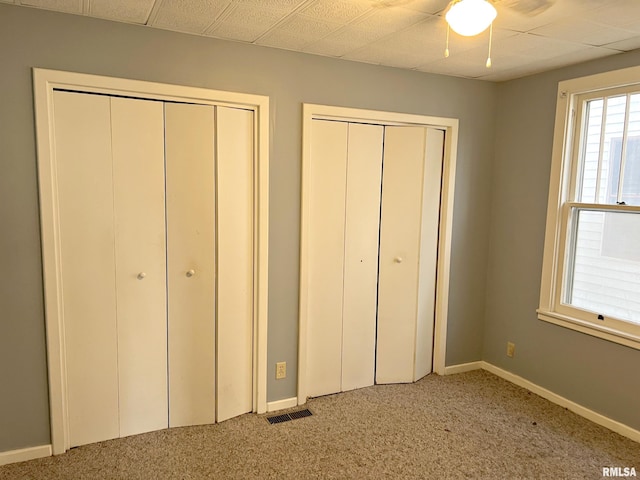 unfurnished bedroom featuring baseboards, visible vents, a ceiling fan, light colored carpet, and multiple closets