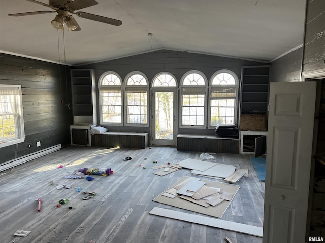 unfurnished living room with lofted ceiling, baseboard heating, ceiling fan, wooden walls, and wood finished floors