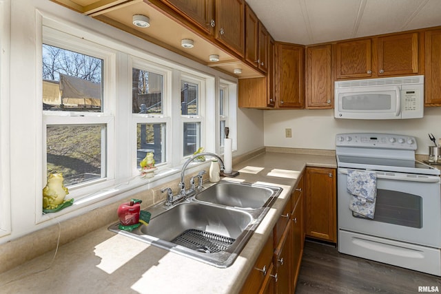 kitchen with white appliances, brown cabinetry, a sink, and light countertops