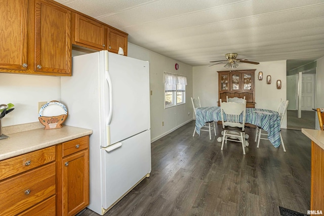 kitchen with dark wood-style flooring, light countertops, brown cabinetry, freestanding refrigerator, and a ceiling fan