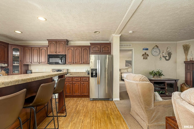 kitchen with black microwave, visible vents, a kitchen breakfast bar, light countertops, and stainless steel fridge