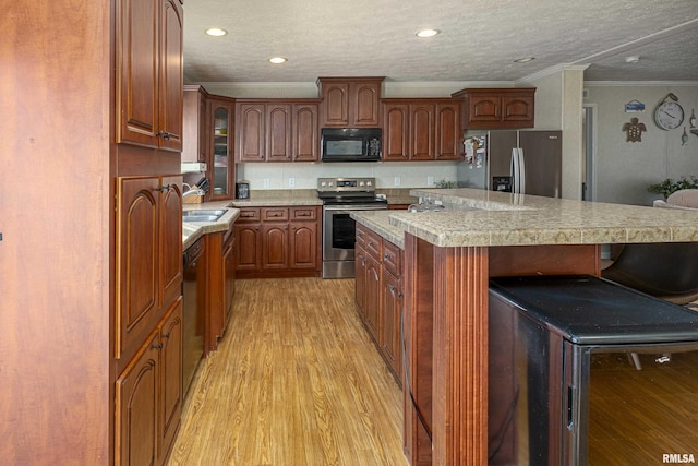 kitchen with light countertops, light wood-style flooring, appliances with stainless steel finishes, a sink, and a kitchen breakfast bar