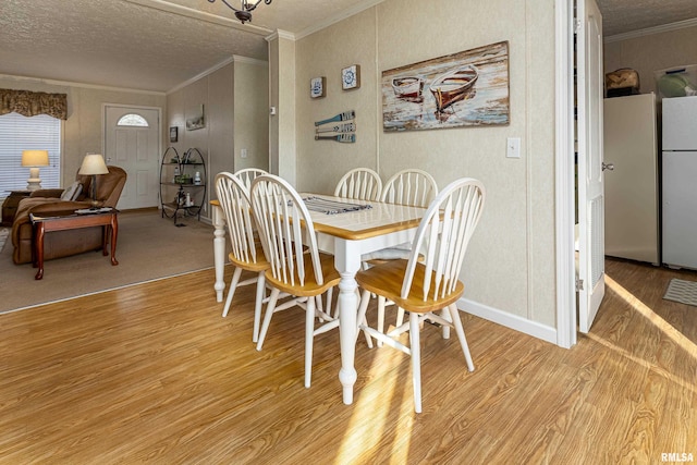 dining space with a textured ceiling, light wood finished floors, baseboards, and crown molding