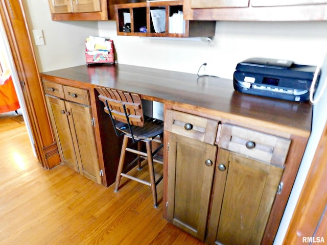 kitchen featuring dark countertops, light wood-style flooring, brown cabinets, and built in desk