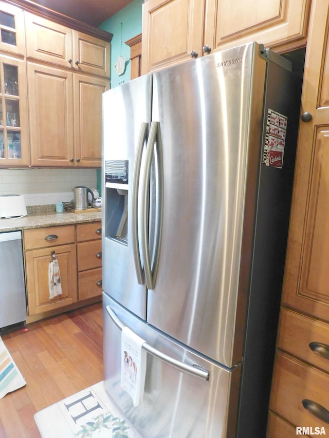 kitchen featuring light wood finished floors, glass insert cabinets, stainless steel appliances, light brown cabinets, and backsplash