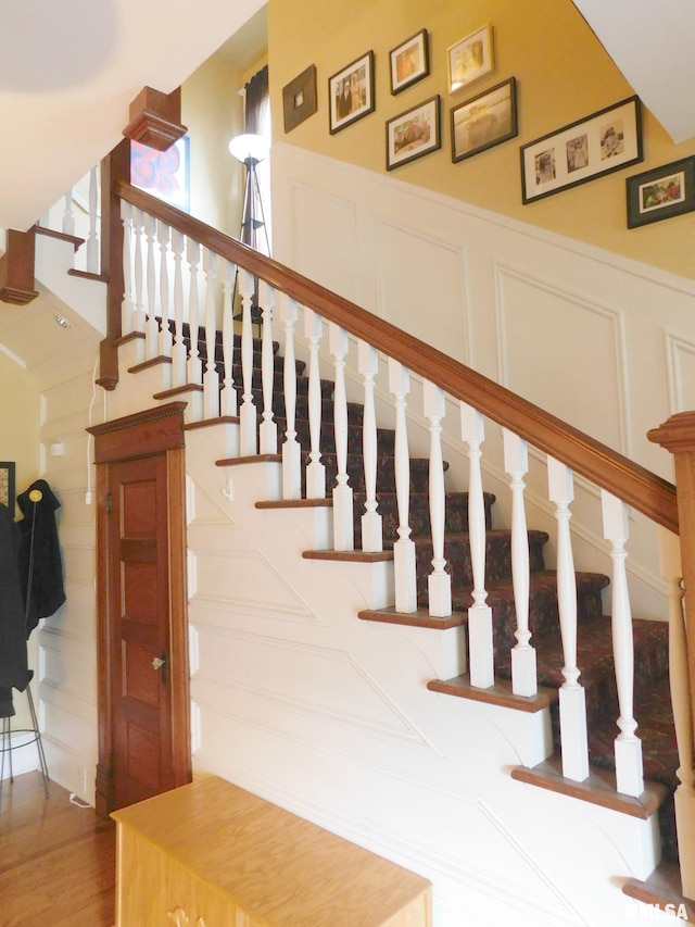 stairway featuring a decorative wall, wood finished floors, and wainscoting