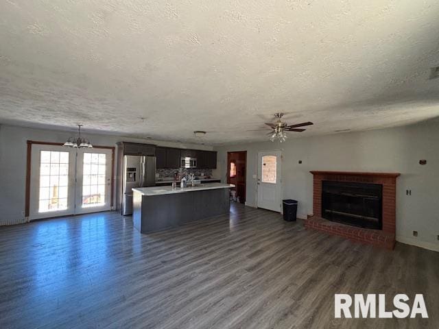 unfurnished living room with a brick fireplace, a textured ceiling, dark wood-type flooring, and ceiling fan with notable chandelier