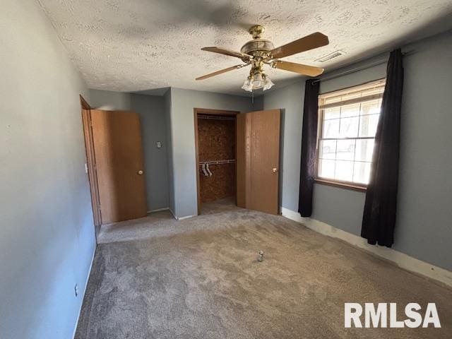 unfurnished bedroom featuring a textured ceiling, carpet floors, visible vents, a ceiling fan, and a closet