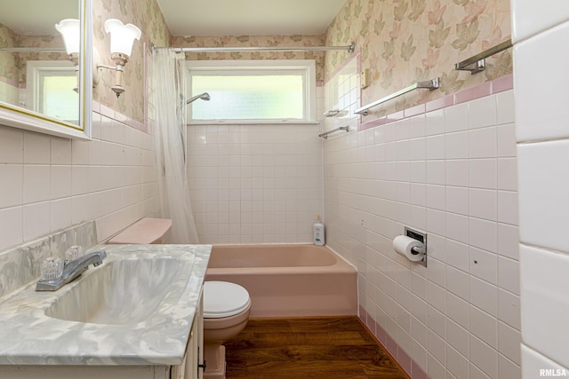 bathroom with toilet, wood finished floors, vanity, tile walls, and shower / bath combo with shower curtain