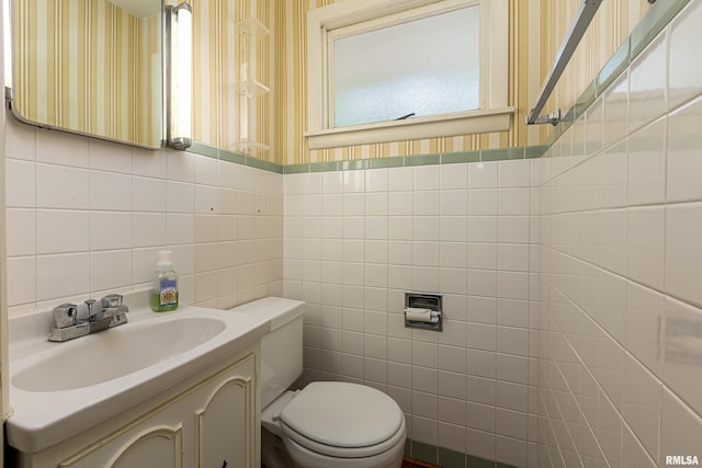 bathroom with wallpapered walls, vanity, toilet, and tile walls