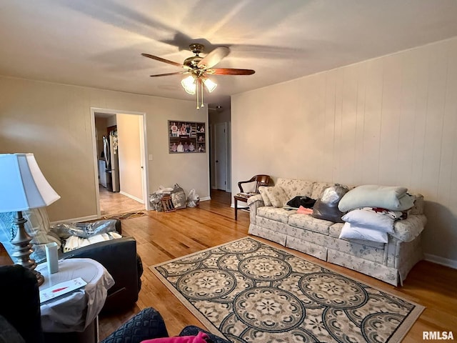 living room with ceiling fan, baseboards, and wood finished floors