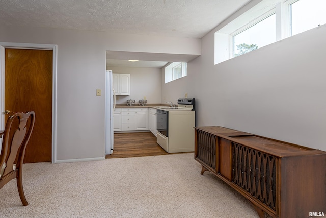 kitchen with white cabinets, light carpet, a textured ceiling, white appliances, and baseboards