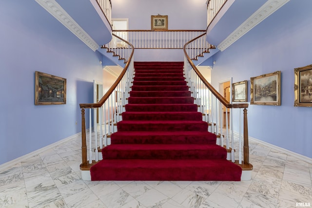 staircase featuring a towering ceiling, marble finish floor, and baseboards