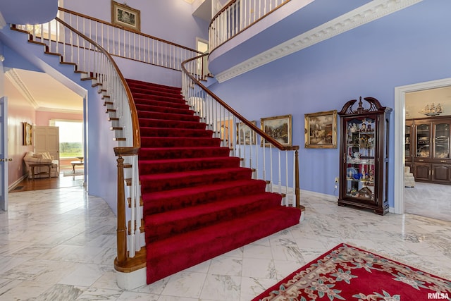 stairway with baseboards, marble finish floor, a towering ceiling, and crown molding