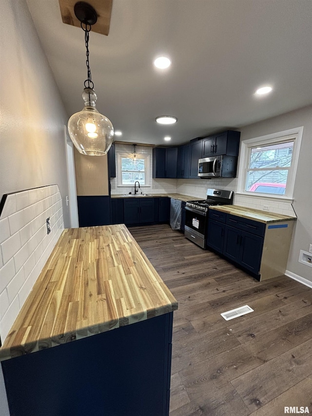 kitchen featuring dark wood-style floors, stainless steel appliances, tasteful backsplash, a sink, and blue cabinets