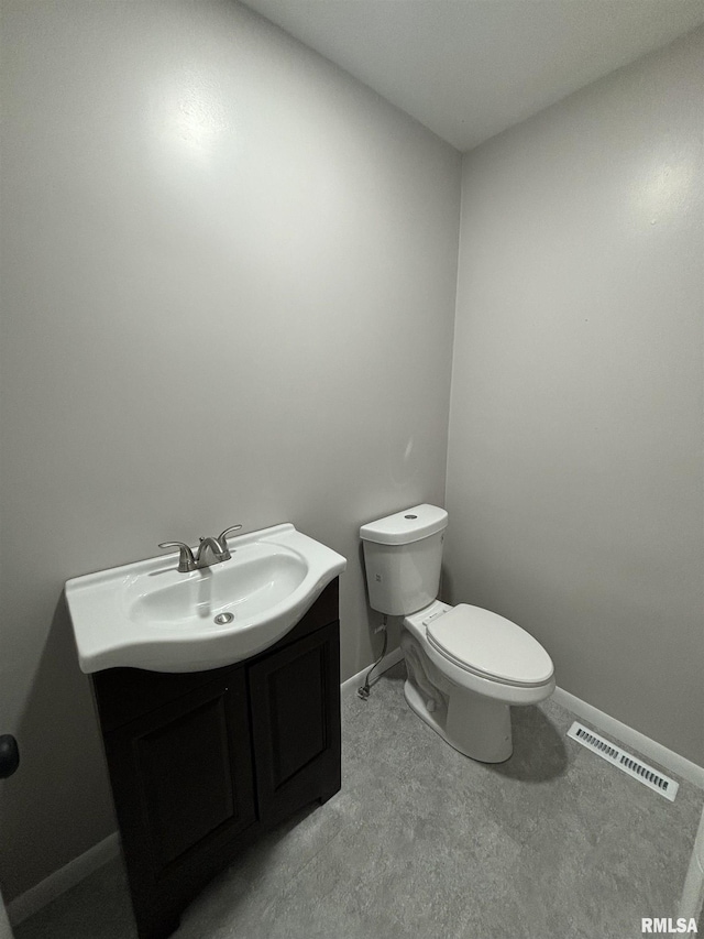 half bath with baseboards, visible vents, vanity, and toilet