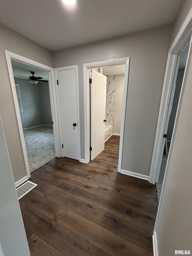 corridor with visible vents, baseboards, and dark wood-style flooring