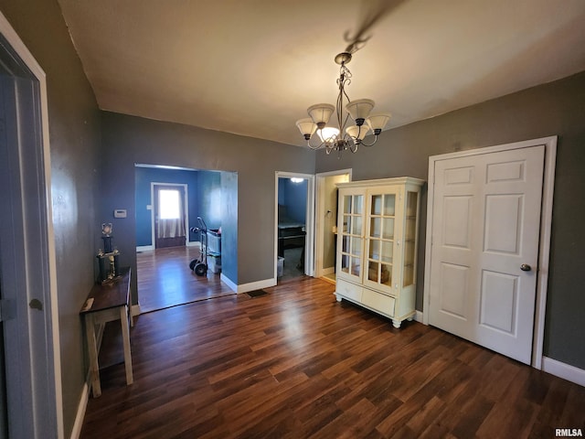 unfurnished dining area featuring dark wood-type flooring, a notable chandelier, and baseboards