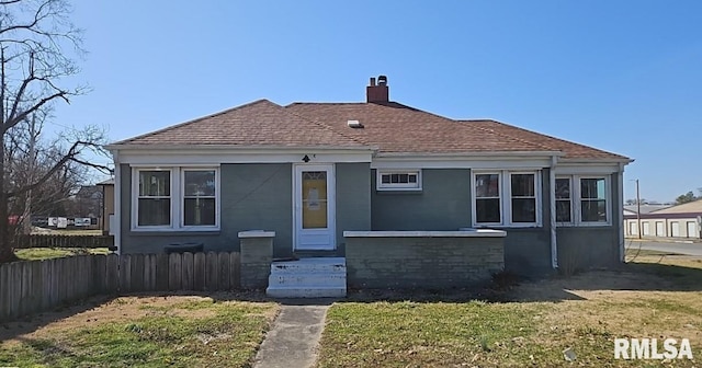 view of front of home with a shingled roof, a chimney, fence, and a front yard