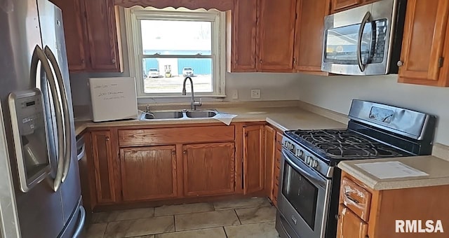 kitchen featuring appliances with stainless steel finishes, brown cabinets, light countertops, and a sink