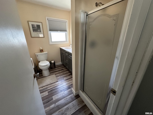 full bath featuring toilet, wood finished floors, vanity, baseboards, and a shower stall