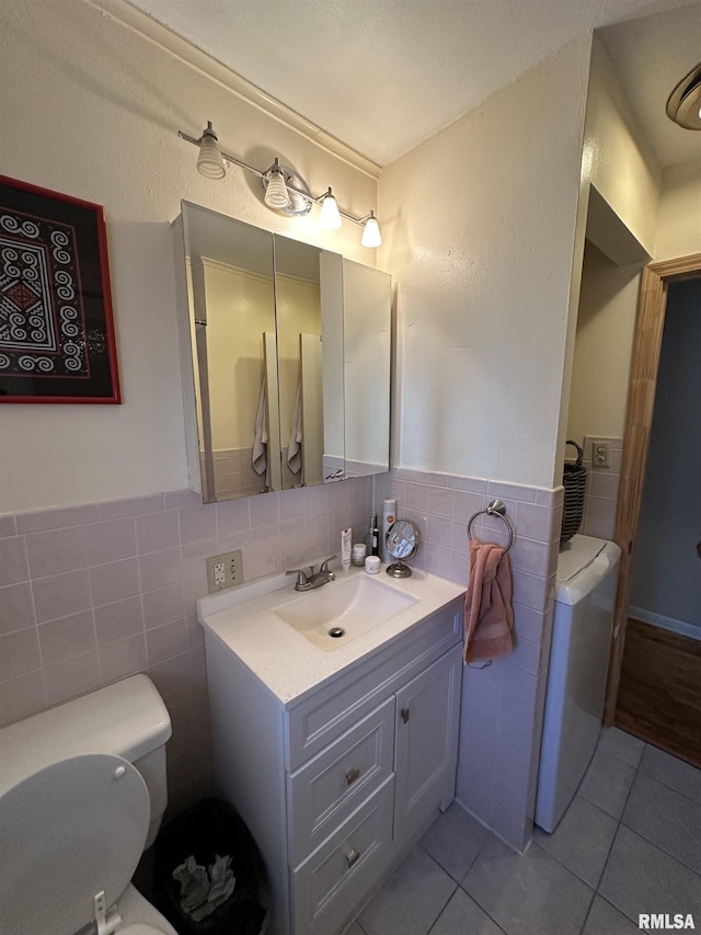 bathroom with toilet, a wainscoted wall, washer / clothes dryer, tile patterned floors, and tile walls