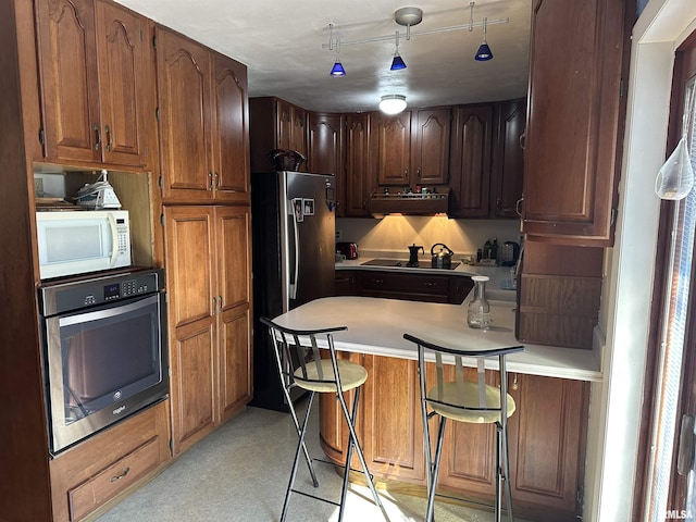 kitchen with a peninsula, light countertops, appliances with stainless steel finishes, ventilation hood, and a kitchen bar